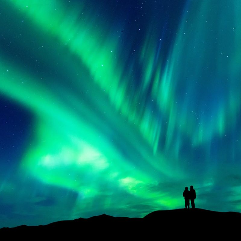 The northern lights above a couple admiring them.