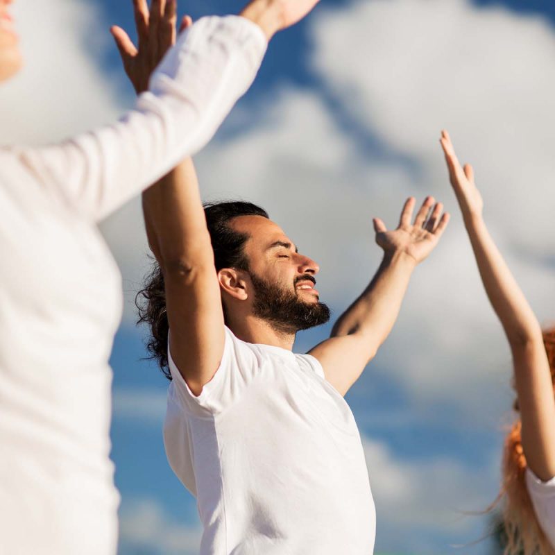 People standing with their arms in the air outdoors in meditation.
