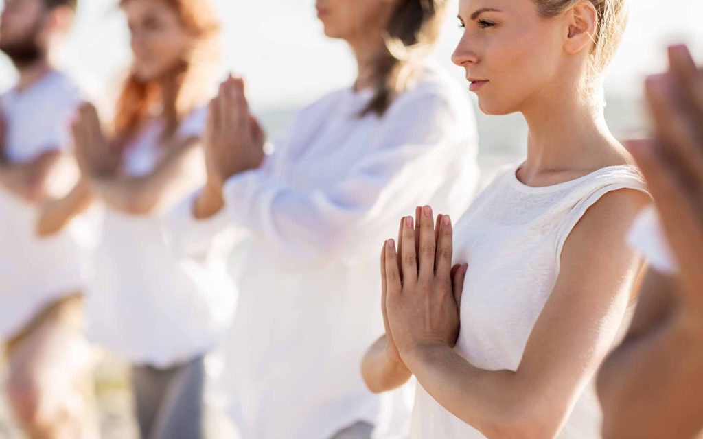 People with their hands clasped in meditation outdoors.