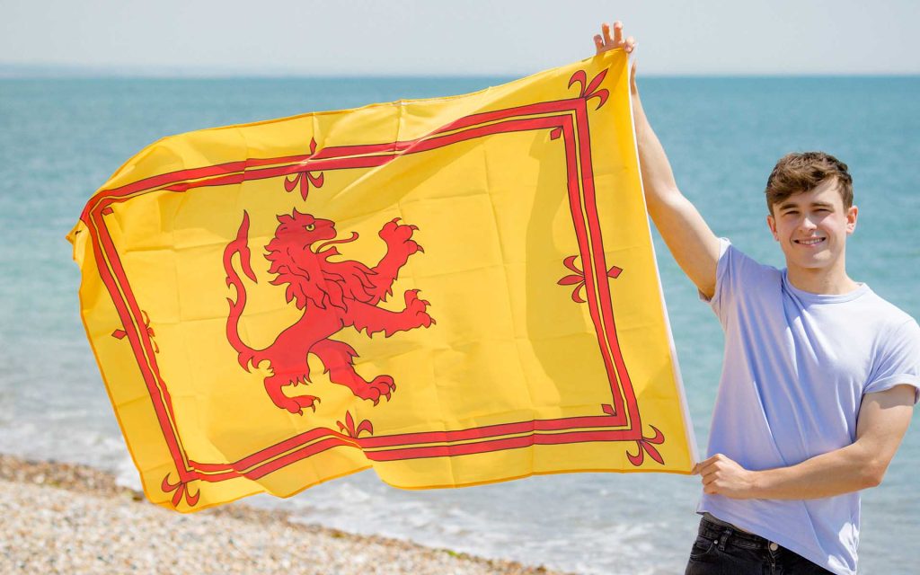 A smiling boy raises the Scottish banner at a beach.