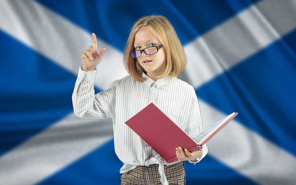 A girl reading a book in front of a Scottish saltire flag.