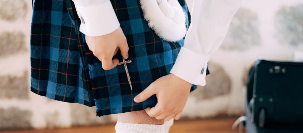 A Scottish groom adds his kilt pin to his Scottish wedding day kilt.