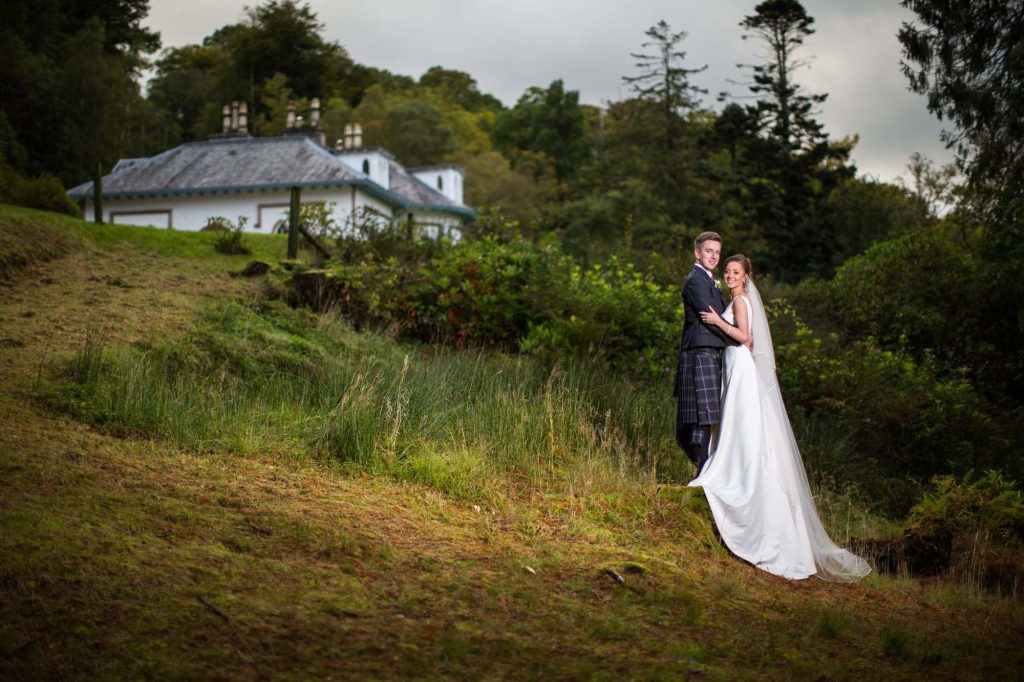 A bride and groom in the grounds of Stuckgowan by Loch Lomond with Stuckgowan in the background