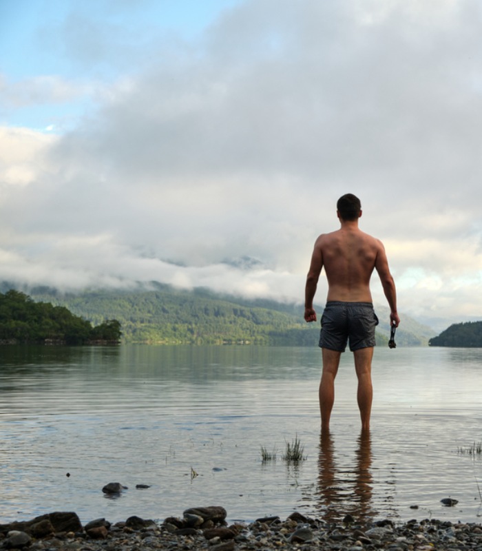 A male wild swimmer stands on the edge of Loch Lomond.