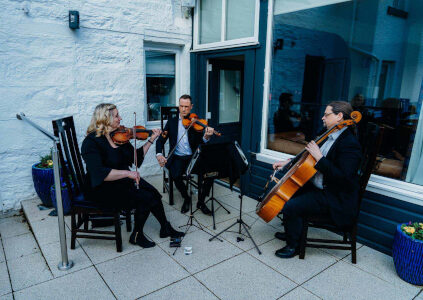 A cello player and two violinists playing on the terrace at a wedding at Stucktaymore next to Loch Tay